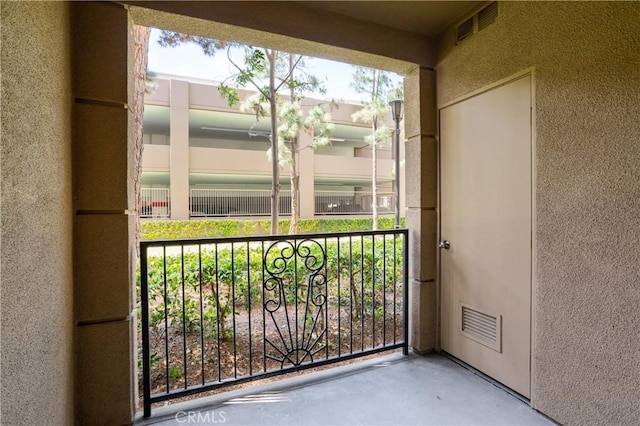view of exterior entry with visible vents, stucco siding, and a balcony