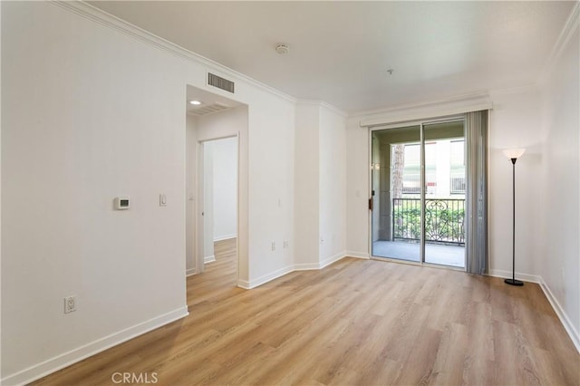 empty room with baseboards, visible vents, light wood-style floors, and crown molding