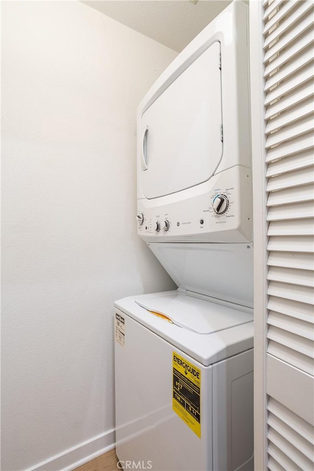 laundry area with baseboards, stacked washer / dryer, and laundry area