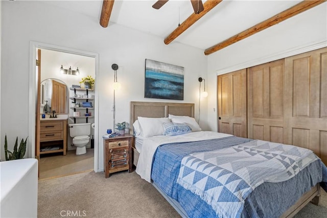 bedroom with a closet, ensuite bathroom, a ceiling fan, beam ceiling, and carpet
