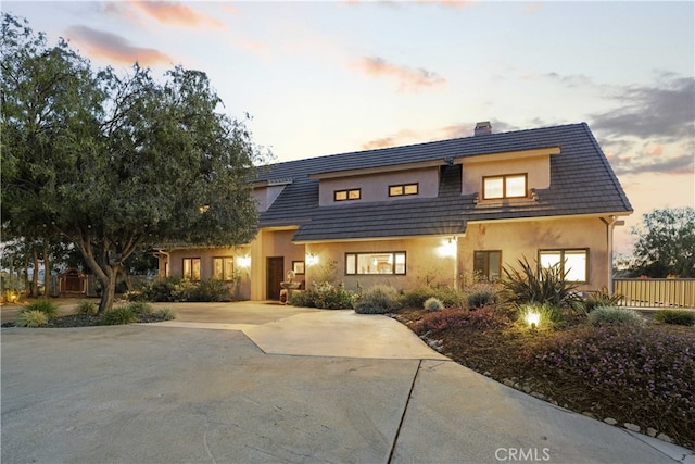 view of front of house with a tiled roof, stucco siding, fence, a chimney, and concrete driveway