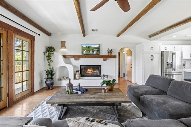 living area featuring a glass covered fireplace, arched walkways, light wood-style floors, and beamed ceiling