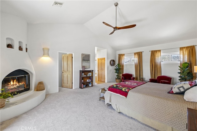carpeted bedroom featuring ensuite bathroom, high vaulted ceiling, ceiling fan, a glass covered fireplace, and visible vents