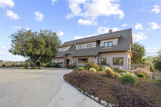 view of front of house featuring a tiled roof, concrete driveway, stucco siding, and a chimney