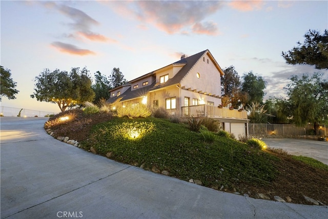 property exterior at dusk with fence, a garage, driveway, and stucco siding