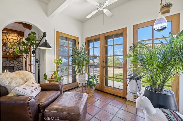 interior space with beamed ceiling, a fireplace, a ceiling fan, tile patterned flooring, and french doors