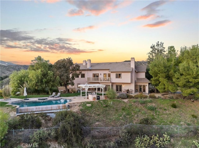 rear view of property with stucco siding, a patio area, fence, a balcony, and a chimney
