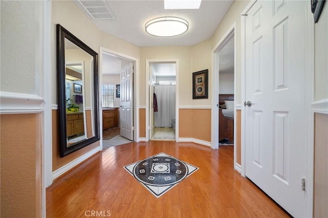corridor with wood finished floors, visible vents, and baseboards