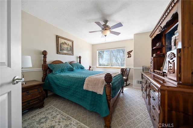 bedroom with light carpet, visible vents, a textured ceiling, and ceiling fan