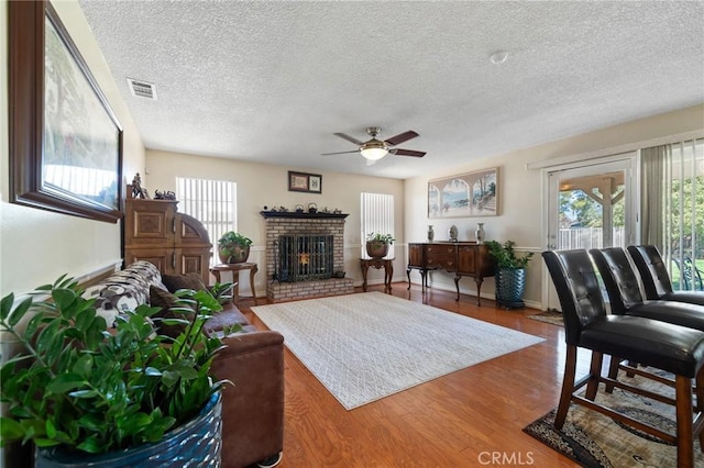 living room featuring a ceiling fan, wood finished floors, visible vents, a fireplace, and a textured ceiling