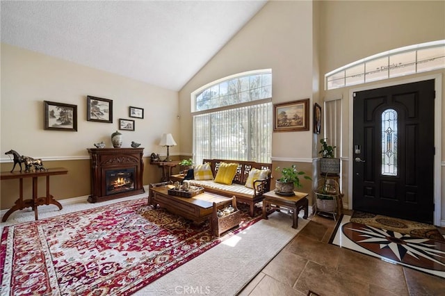 foyer featuring a glass covered fireplace, high vaulted ceiling, and baseboards