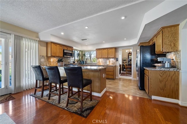 kitchen with stainless steel microwave, brown cabinets, a peninsula, and light wood-style flooring