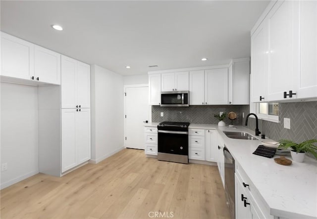 kitchen featuring backsplash, appliances with stainless steel finishes, a sink, and light wood-type flooring