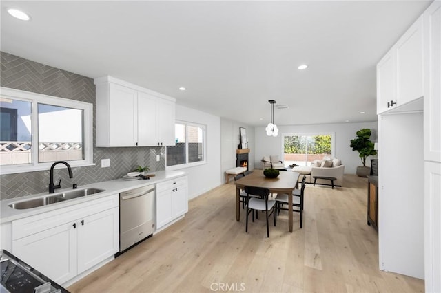 kitchen featuring light countertops, white cabinets, a sink, light wood finished floors, and dishwasher