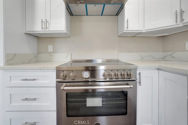 kitchen with high end stainless steel range oven, white cabinets, exhaust hood, and light stone counters