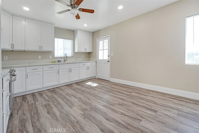 kitchen featuring white cabinets, baseboards, a ceiling fan, and a sink