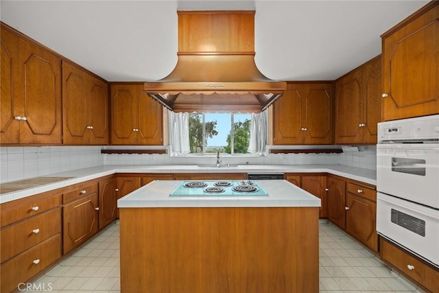 kitchen featuring backsplash, a center island, brown cabinetry, white appliances, and a sink