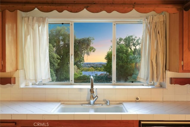 kitchen with tasteful backsplash, tile countertops, dishwasher, and a sink