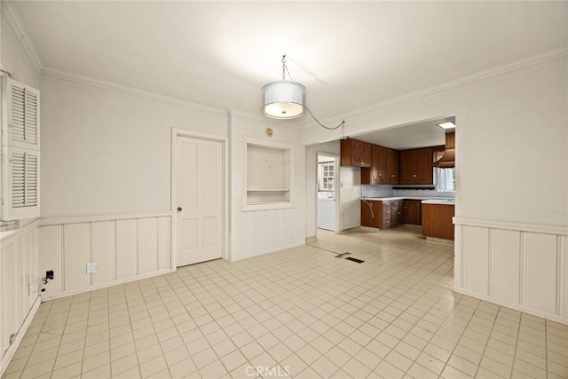 kitchen with light countertops, a decorative wall, crown molding, and wainscoting