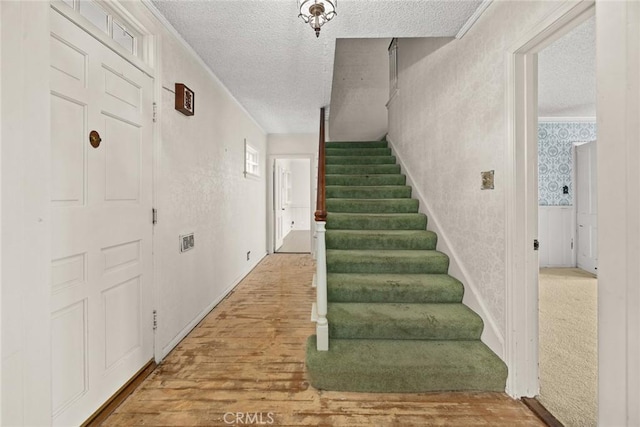 staircase featuring a textured ceiling, wood finished floors, and wallpapered walls