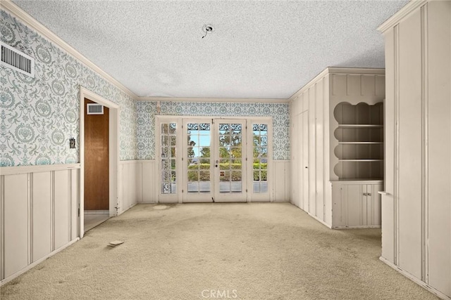 carpeted empty room featuring visible vents, ornamental molding, a textured ceiling, wainscoting, and wallpapered walls