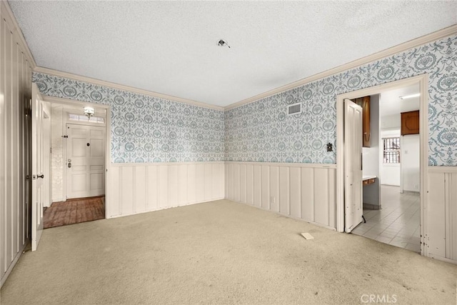 empty room featuring wallpapered walls, a textured ceiling, carpet flooring, and wainscoting