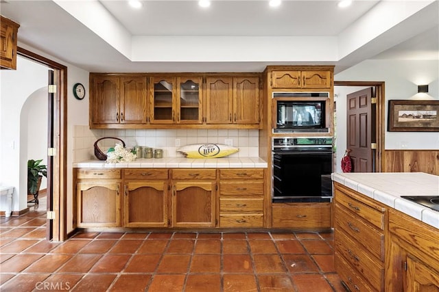 13155 San Antonio Rd, Atascadero, CA 93422 - kitchen with black appliances, arched walkways, tasteful backsplash, brown cabinets, and tile counters