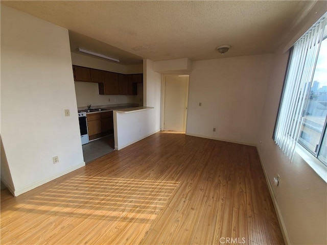 unfurnished living room with a textured ceiling, light wood-type flooring, baseboards, and a sink