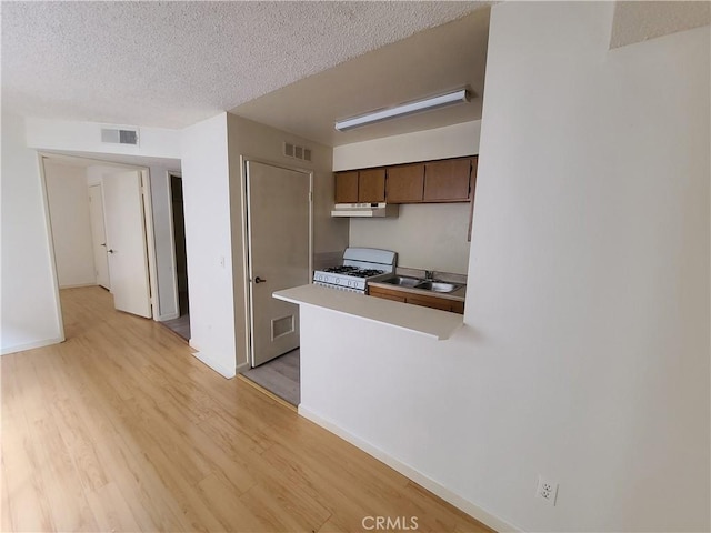 kitchen with white gas stove, light wood-style floors, visible vents, and a textured ceiling