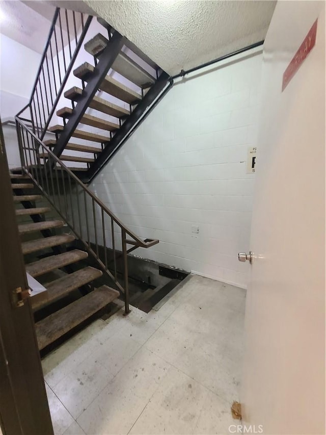 stairway with a textured ceiling and concrete block wall