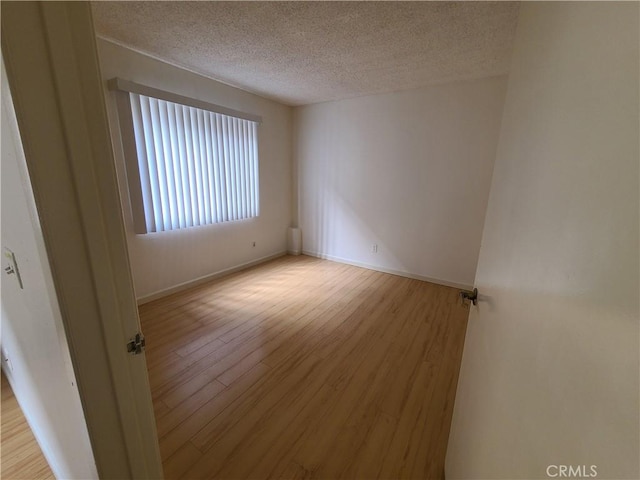 spare room featuring baseboards, a textured ceiling, and wood finished floors