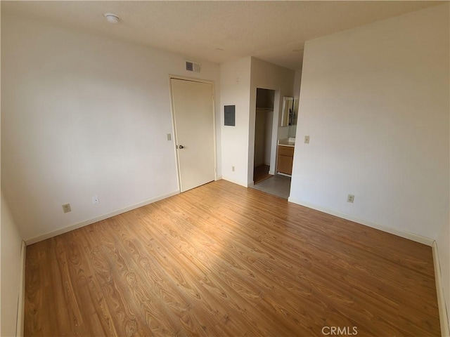 empty room with electric panel, wood finished floors, visible vents, and baseboards