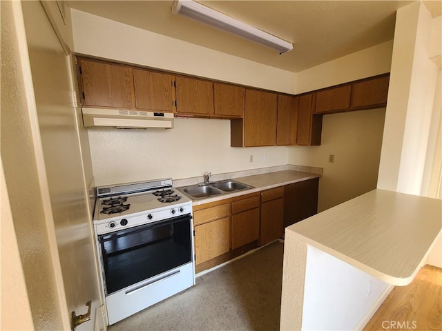 kitchen featuring brown cabinets, under cabinet range hood, a sink, light countertops, and white range with gas stovetop