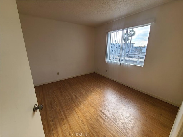 unfurnished room featuring a textured ceiling, baseboards, and wood finished floors