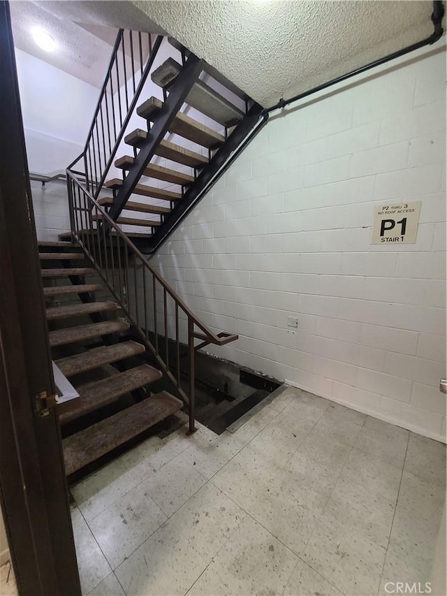 stairs with tile patterned floors, a textured ceiling, and concrete block wall