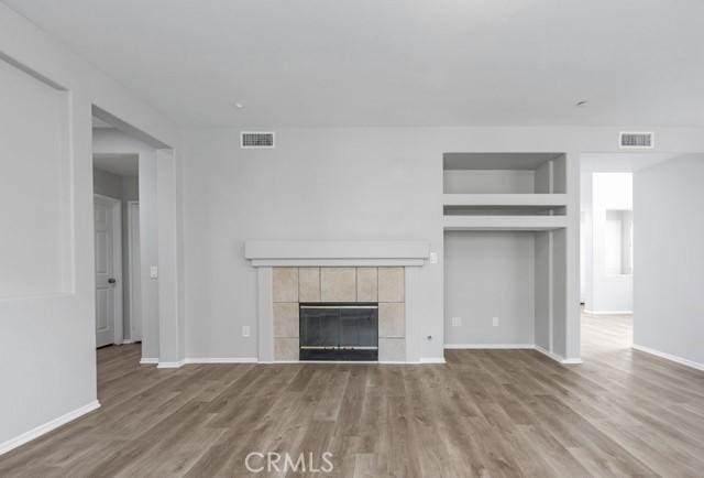 unfurnished living room featuring visible vents, a fireplace, baseboards, and wood finished floors