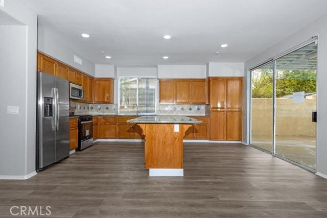 kitchen with dark wood finished floors, backsplash, stainless steel appliances, and a kitchen bar