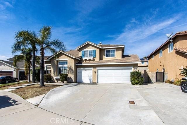 traditional-style home with a tiled roof, concrete driveway, stucco siding, an attached garage, and a gate