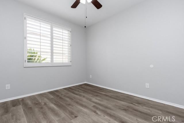 empty room with wood finished floors, a ceiling fan, and baseboards