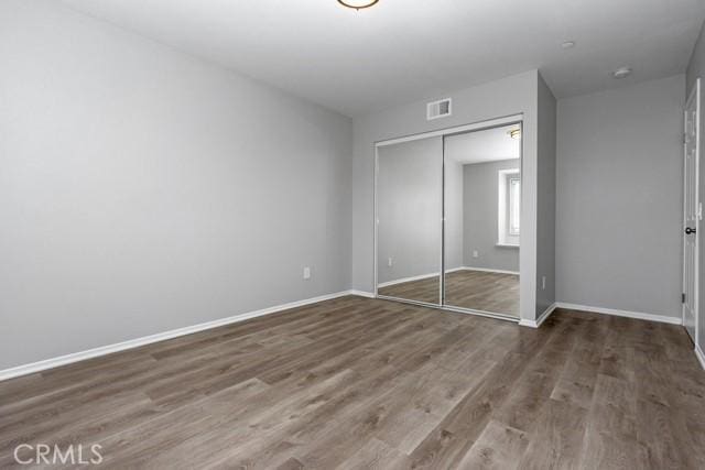 unfurnished bedroom with visible vents, baseboards, a closet, and wood finished floors