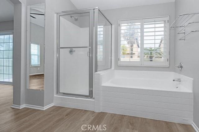 bathroom featuring a shower stall, a bath, wood finished floors, and baseboards