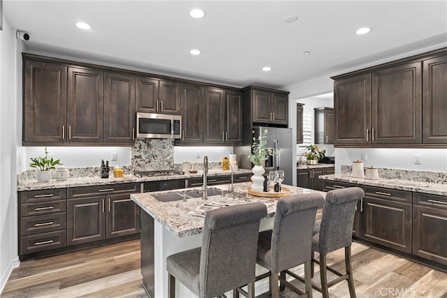 kitchen with stainless steel appliances, a sink, dark brown cabinetry, light wood-style floors, and a breakfast bar