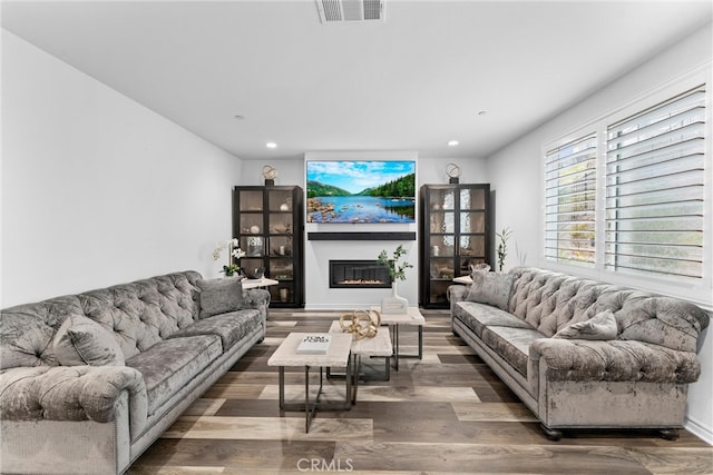 living area featuring a glass covered fireplace, wood finished floors, visible vents, and recessed lighting