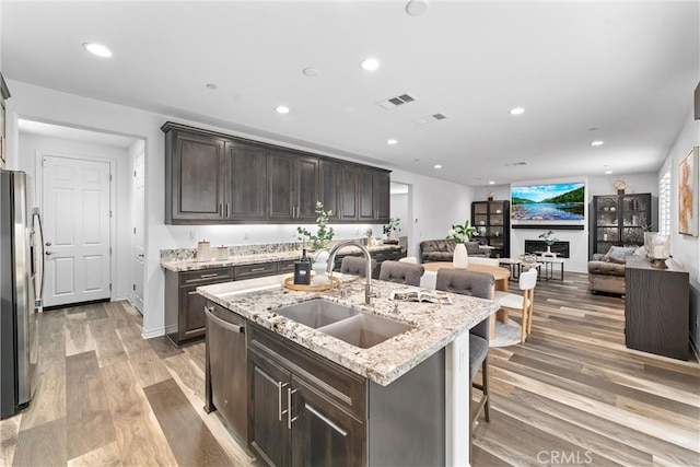 kitchen featuring dark brown cabinets, a sink, open floor plan, appliances with stainless steel finishes, and visible vents