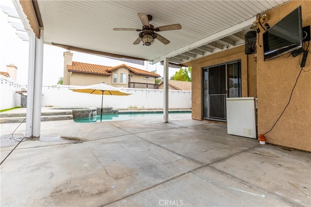 view of patio with a fenced backyard, a ceiling fan, and a pool with connected hot tub