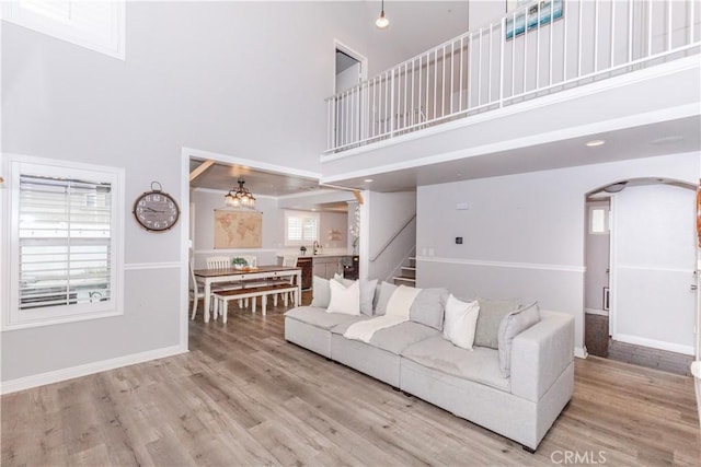 living room featuring a towering ceiling, wood finished floors, baseboards, stairway, and arched walkways
