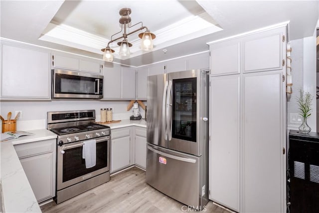 kitchen featuring light wood-type flooring, pendant lighting, appliances with stainless steel finishes, and a tray ceiling