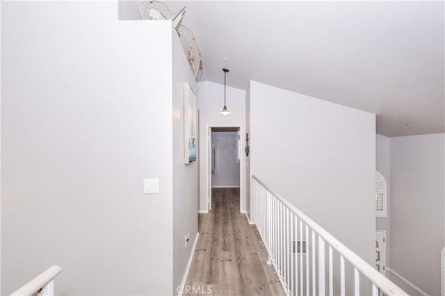 hallway with baseboards, an upstairs landing, and light wood-style flooring