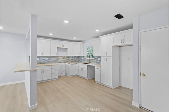 kitchen featuring tasteful backsplash, baseboards, a sink, light wood-type flooring, and white cabinetry