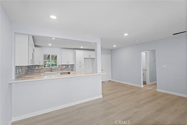 kitchen featuring light wood-type flooring, a peninsula, light countertops, white cabinets, and decorative backsplash